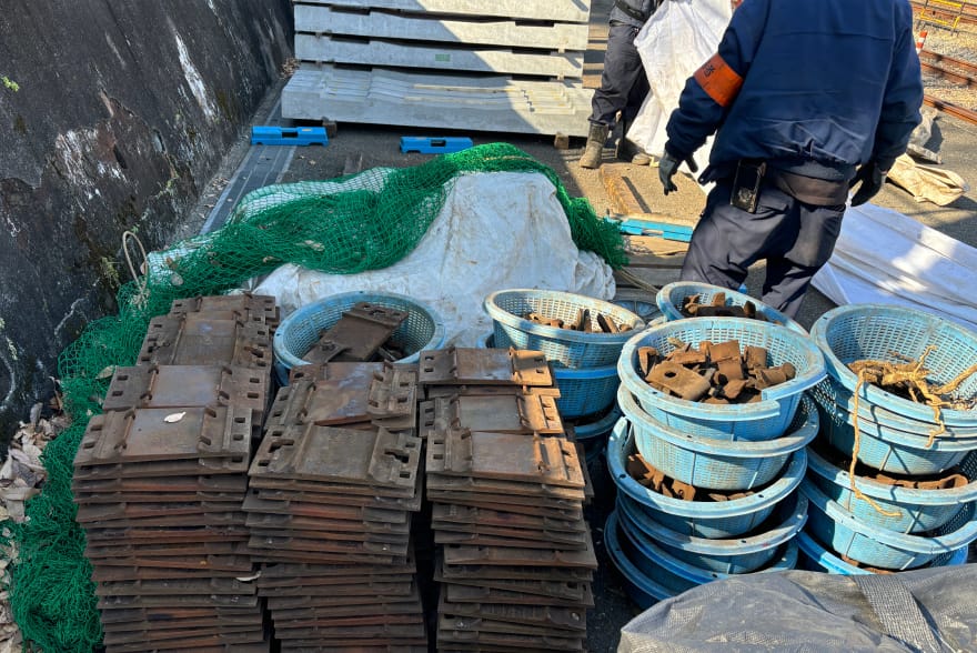 鉄道工事に使われる金属部品が青いかごやパレットに整理されて置かれている