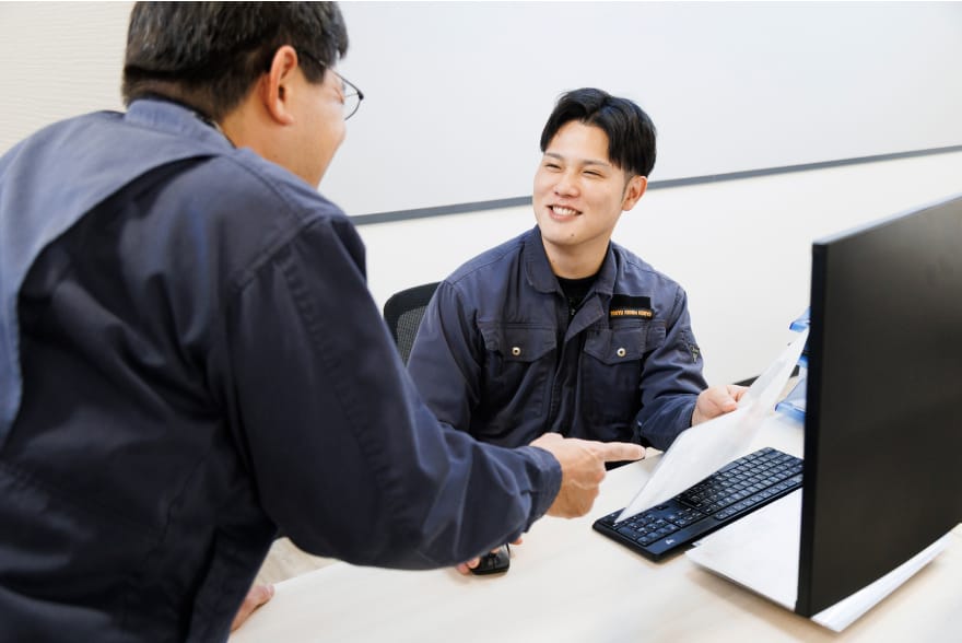 オフィスで作業員が笑顔で会話しながら書類を確認している、明るい雰囲気の打ち合わせ風景