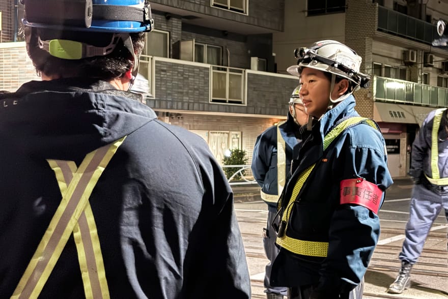 夜間の線路脇で作業員がヘルメットと安全ベストを着用し、責任者として現場の確認を行っている