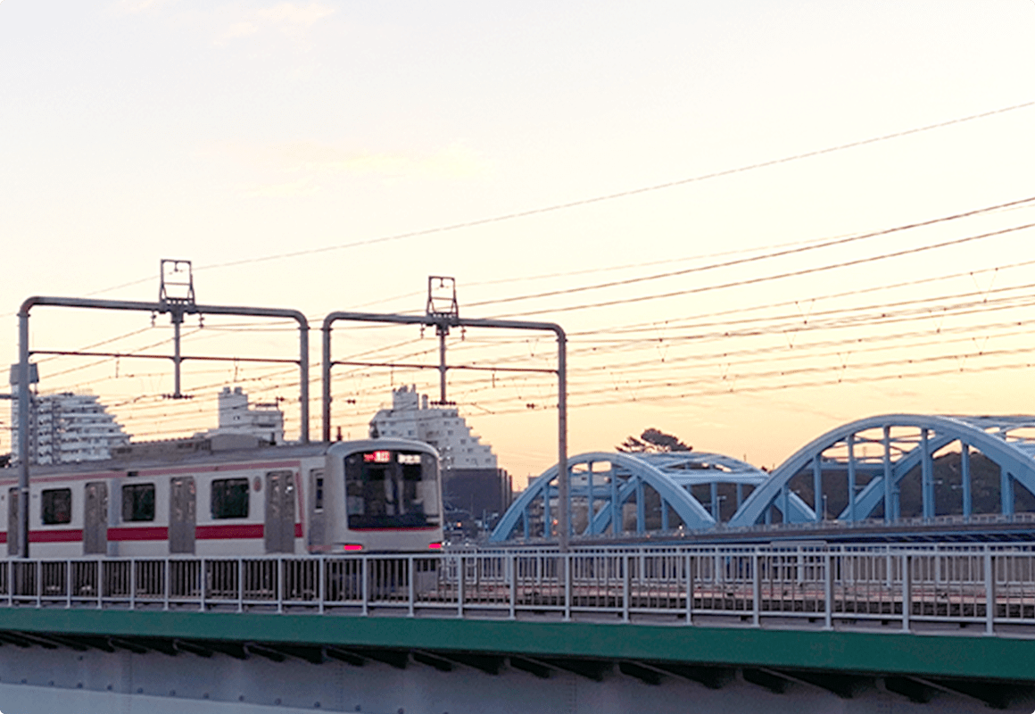 背景には高層マンションと夕焼け空が広がり、手前には鉄橋を走行する電車が写っている
