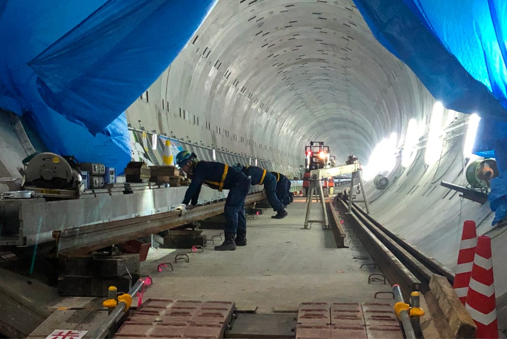 トンネル内で作業員がレールの設置や調整を行っている工事現場の一場面