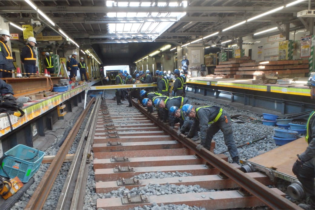 駅構内で多数の作業員が連携して線路の補修・点検を行っている様子